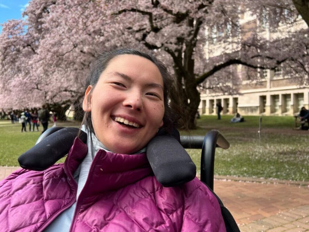 Smiling woman in wheelchair, cherry blossoms.