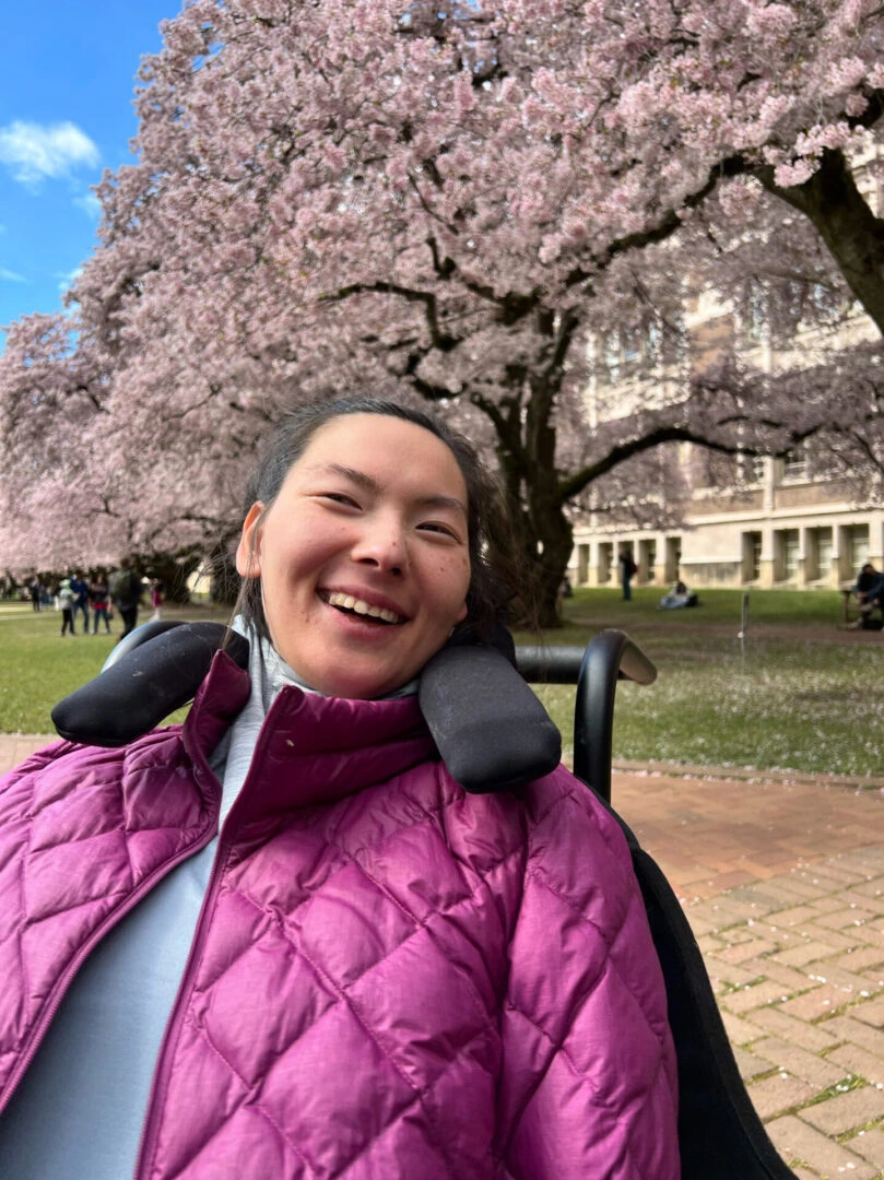 Smiling woman in wheelchair, cherry blossoms.